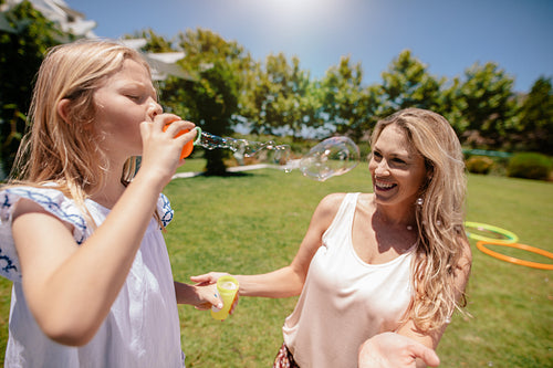 Little girl blowing soap bubbles with her mother in park
