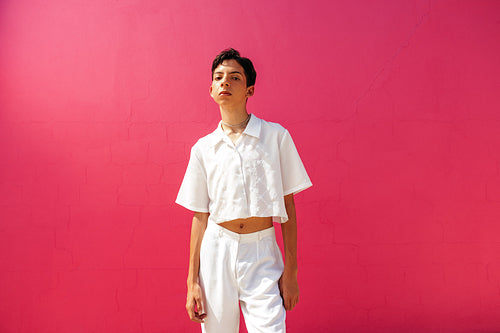 Self-confident queer boy standing against a pink background