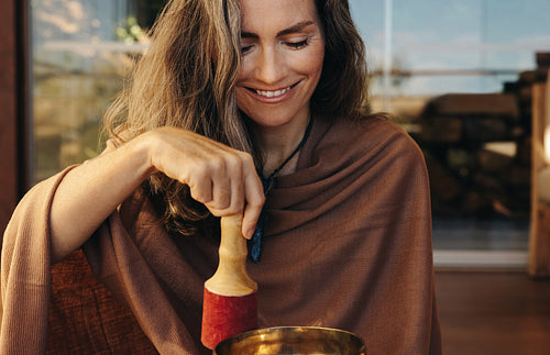 Happy senior woman playing a tibetan singing bowl at home