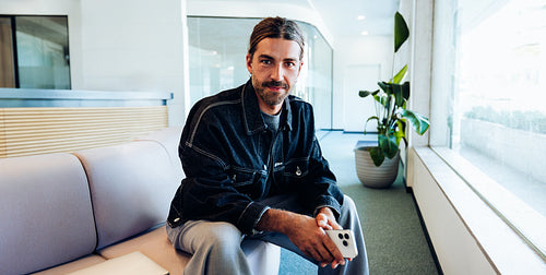 Man waiting in office lobby with smartphone
