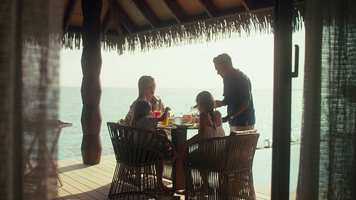 Family enjoys breakfast together on an overwater villa deck at a tropical resort