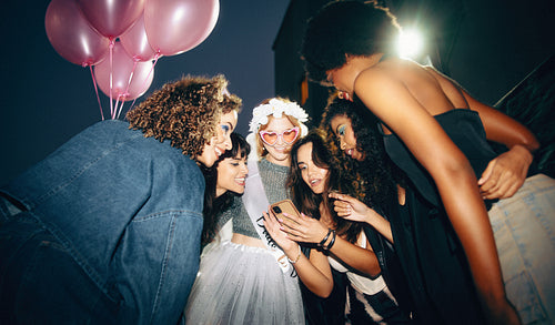 Bachelorette party friends celebrating with balloons and sharing moments on a smartphone