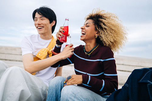 Friends laughing and clinking soda bottles outdoors