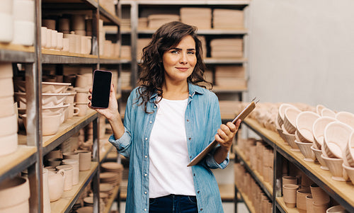 Female ceramist showing a blank smartphone screen in her shop