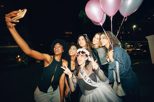 Group of friends celebrating with balloons and taking a selfie at night