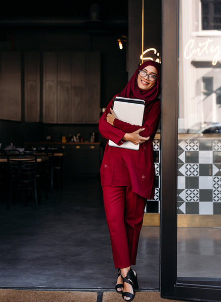 Muslim woman standing with laptop at coffee shop door