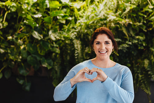 Happy business woman showing a heart gesture while standing in a green office