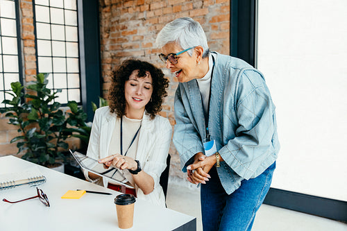 Colleagues engaged in a collaborative discussion using a tablet in a modern corporate office setting with brick walls and natural light