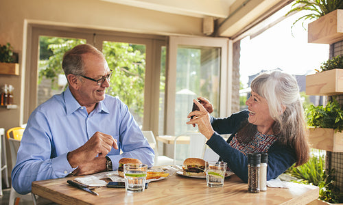 Smiling senior woman taking picture of her husband at restaurant