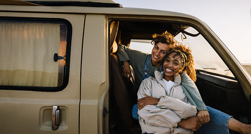 Two friends share a warm moment in a beige van while embracing at sunset