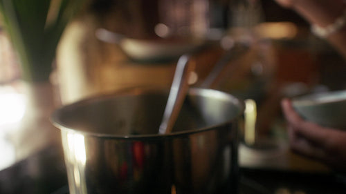 Close-up of a person mixing a pot on the stove with a wooden spoon
