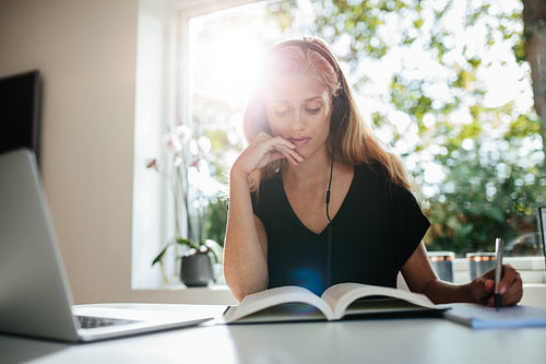 Woman sitting at table with laptop and taking notes