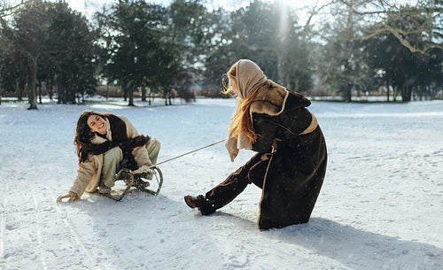 Woman rides a sled while friend pulls through snow