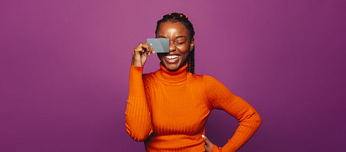 Young woman holding credit card and smiling against purple background