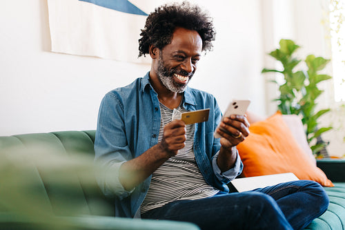 Man using a credit card and a mobile app for online shopping at home