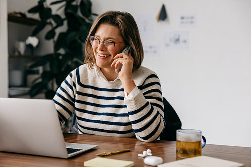On a phone call, the woman keeps working at her laptop in a home office