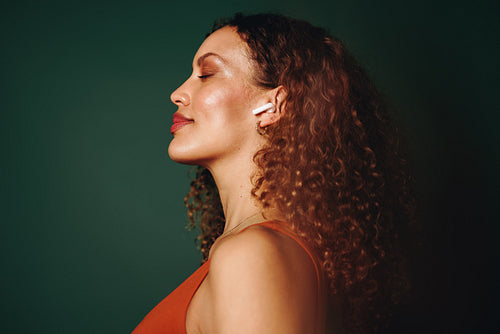 In side view, the woman wears earbuds for a wellness moment in studio