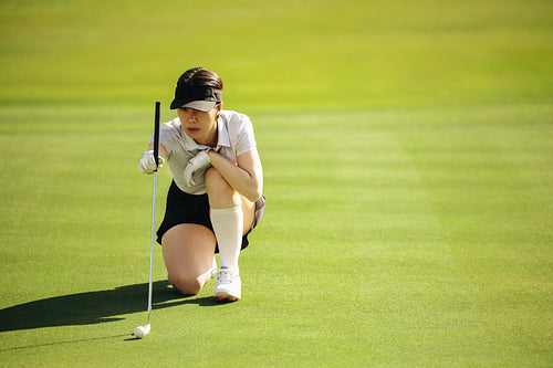 Professional woman golfer focused on the green, preparing for a putt at a golf course.