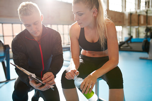 Young woman with her physical trainer looking at fitness plan