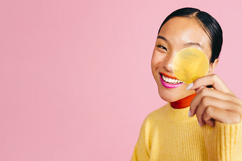 Gorgeous gen z woman smiling at the camera, holding a yellow cap from a cosmetic product