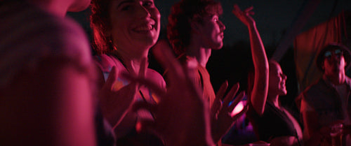 A diverse group of young people dance and laugh while enjoying live music at an outdoor festival at night