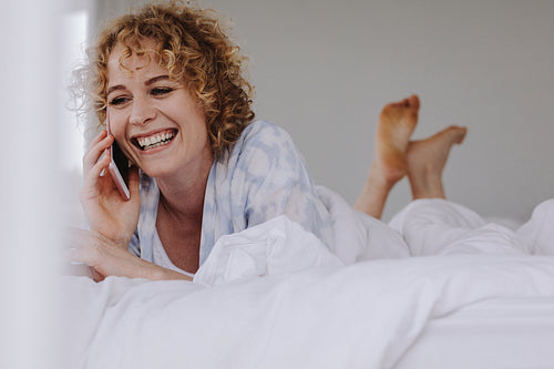 Woman talking on mobile phone lying on bed