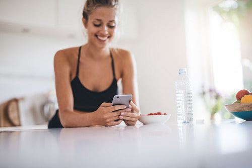 Beautiful young female using mobile phone in kitchen