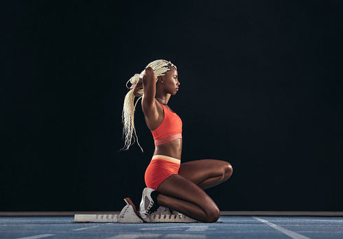 Woman sprinter sitting at the start line on a running track