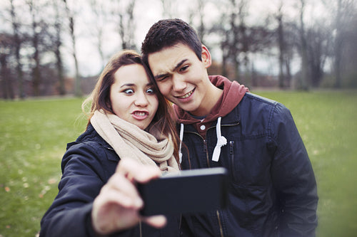 Funny teenage couple photographing themselves with smart phone in the park