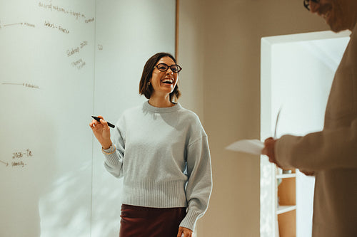 Woman leads brainstorming meeting by the whiteboard in an office with a coworker