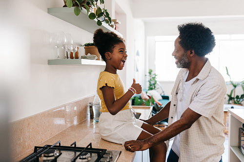 Young girl sharing a fun story with her mature father in the kitchen at home