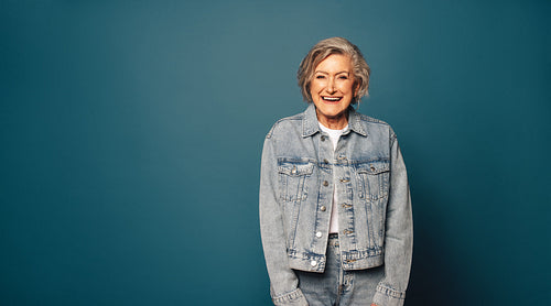 Mature woman in casual clothing laughing and standing against a blue background