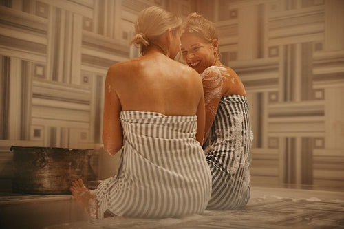 Mature woman and younger woman chatting and laughing in Turkish bath spa