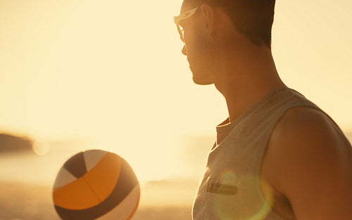 Young athlete playing beach volleyball at sunset
