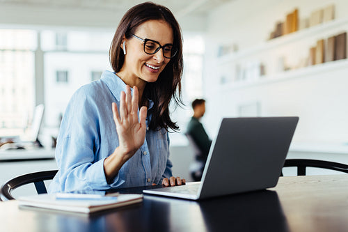 Woman waving on a video call in an office