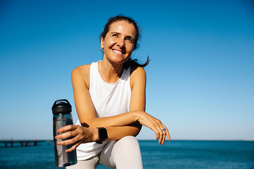 Smiling woman enjoying outdoor fitness with a water bottle and blue sky