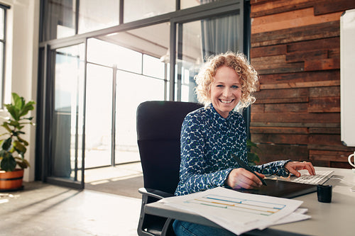 Happy young female graphic designer working at her desk