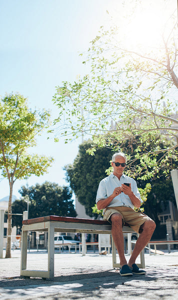 Mature man sitting outdoor in city using mobile phone