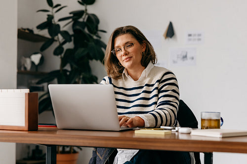 Focused and professional, the woman works on a laptop at her home office desk