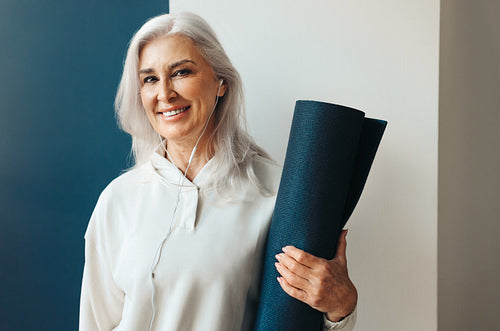 Mature woman holding yoga mat, preparing to find balance in her practice