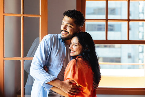 Happy couple embracing near a bright window in their modern apartment