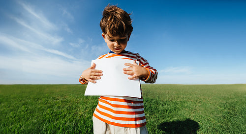 Boy in striped shirt holds blank paper outdoors
