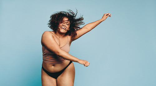 Happy young woman celebrating her body in a studio, having fun in underwear