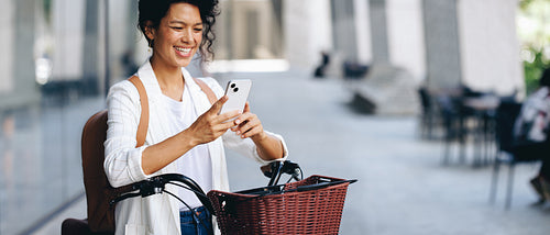 Joyful woman texting on smartphone while riding bicycle in urban European city