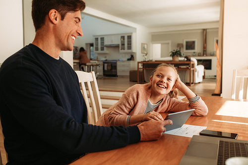 Smiling father and daughter at home with digital tablet
