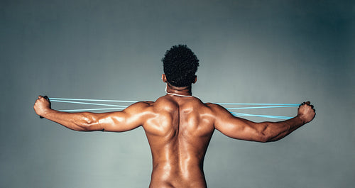 Muscular young man stretching arms with rubber band