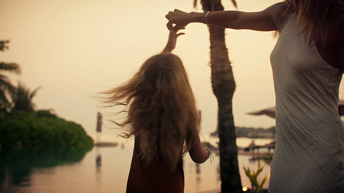 A mother and her daughter enjoy a happy dance by the water at sunset