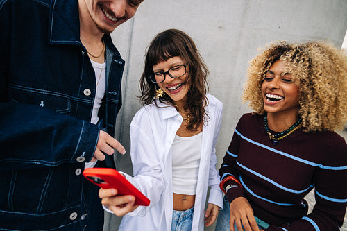 Friends laughing together while looking at smartphone