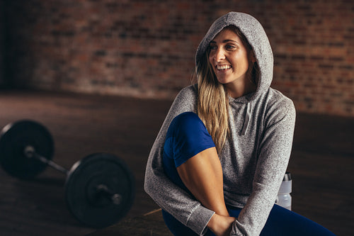Smiling woman in hoodie relaxing at fitness studio