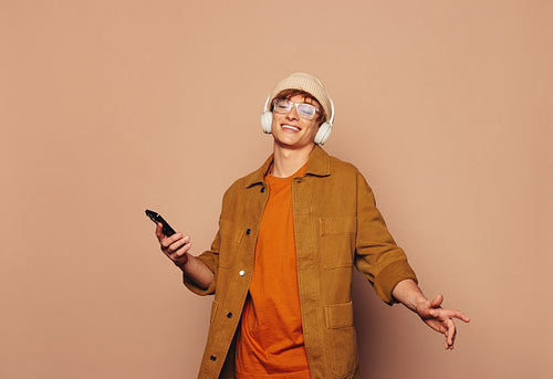 Cheerful man holding a mobile phone and listening to music on a vibrant peach background